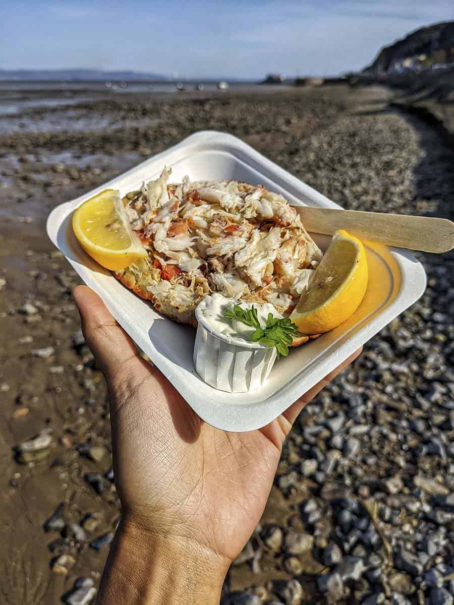 A takeaway box of dressed crab served in its shell with slices of lemon