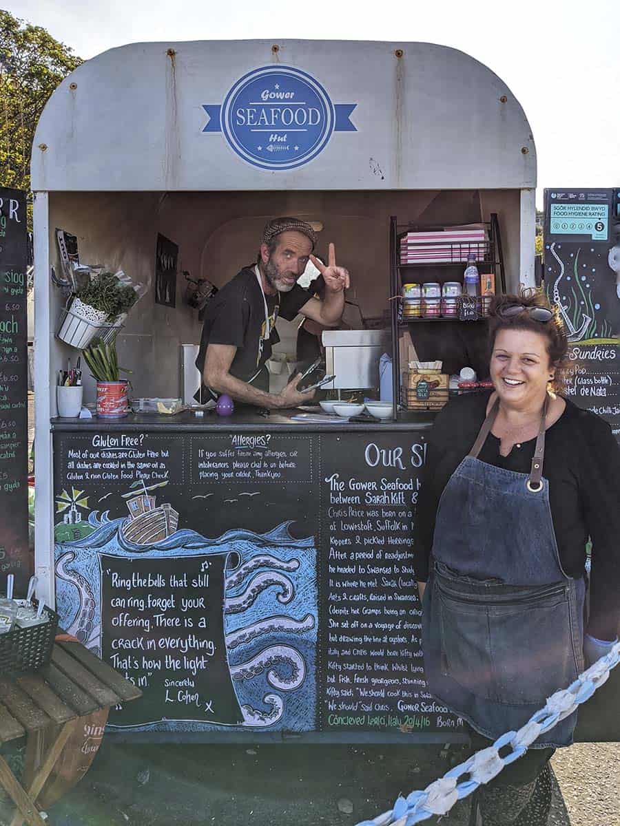 A man and woman selling from a seafood hut smiling at the camera