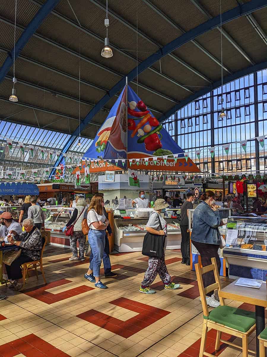 The inside of a spacious and colourful indoor market with large windows, stalls and people