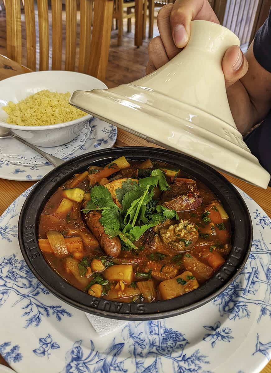 The conical lid of a tagine pot being lifted to reveal the tagine within