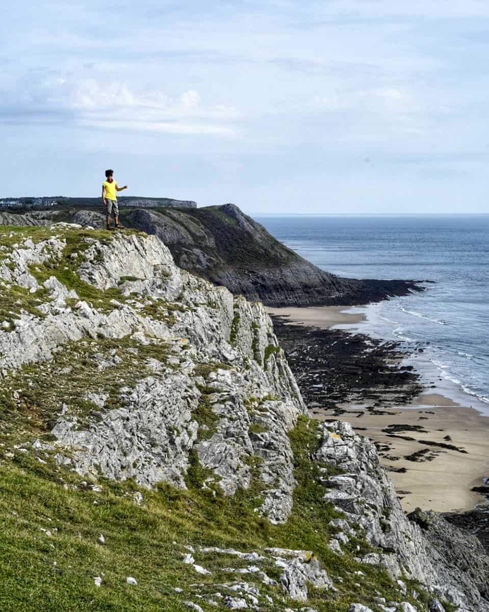 A person in the distance standing on top of a cliff by the sea