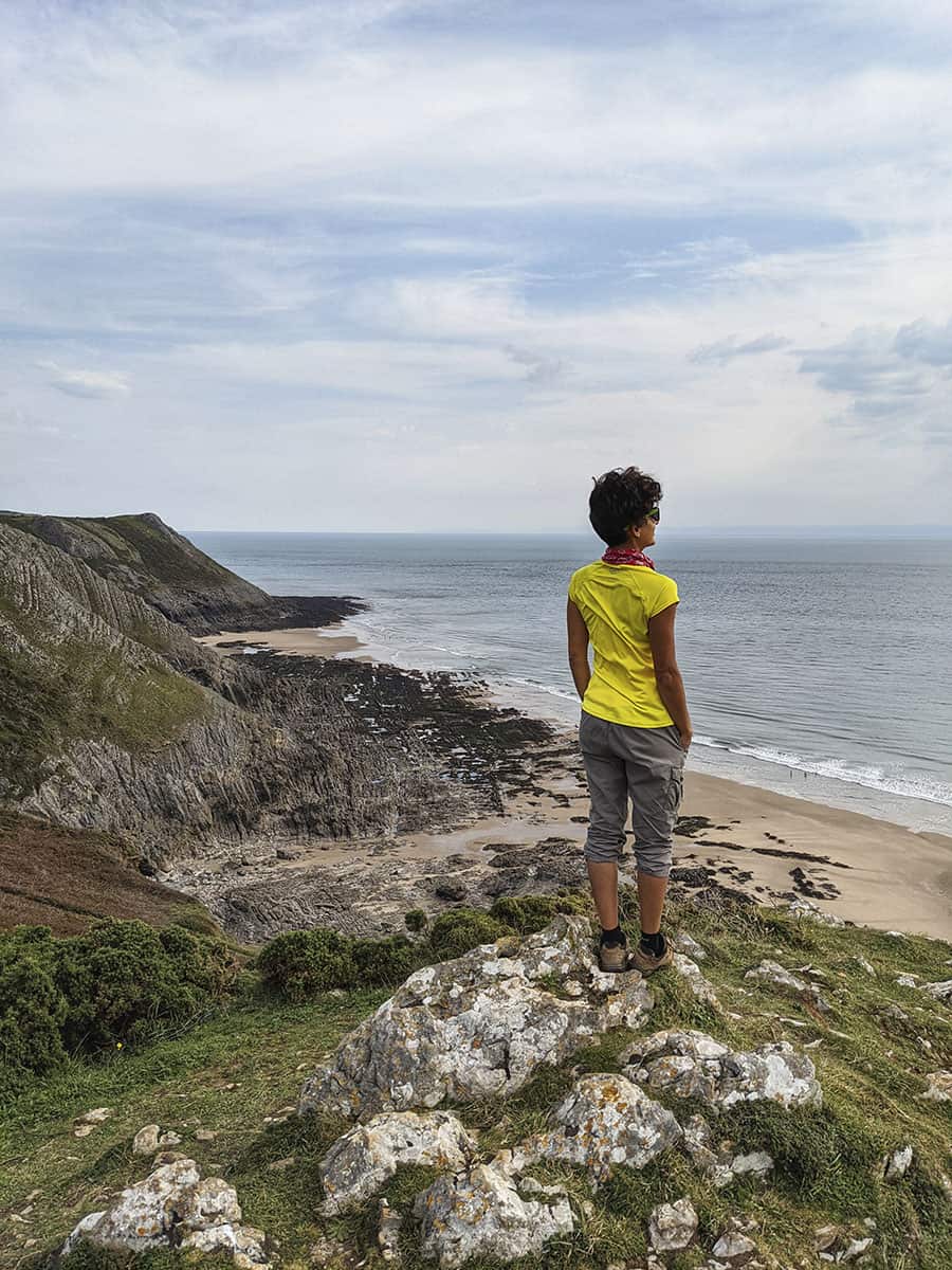 A girl standing on top of a cliff looking out to sea