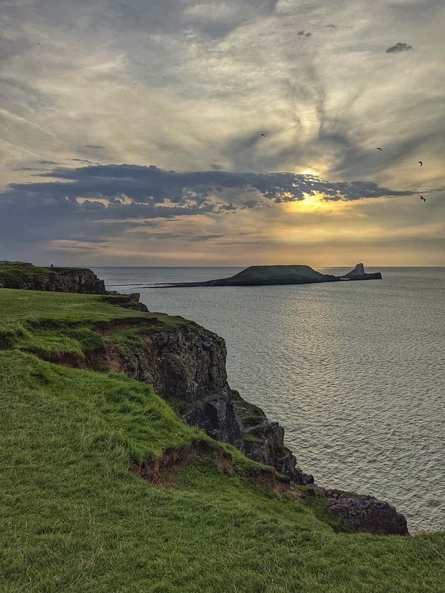 Grass covered cliff tops and the sea at sunset