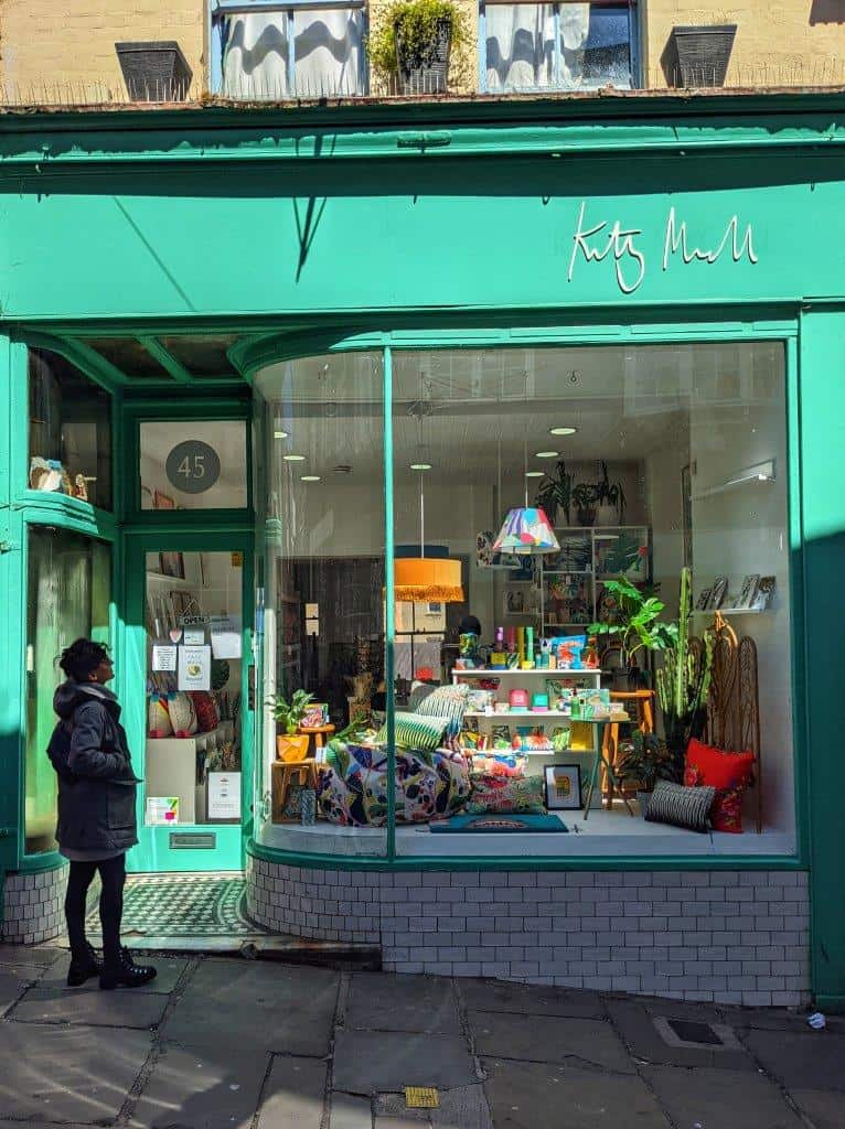 A vibrant mint green shopfront with a girl looking through the window at the colourful homeware items on display