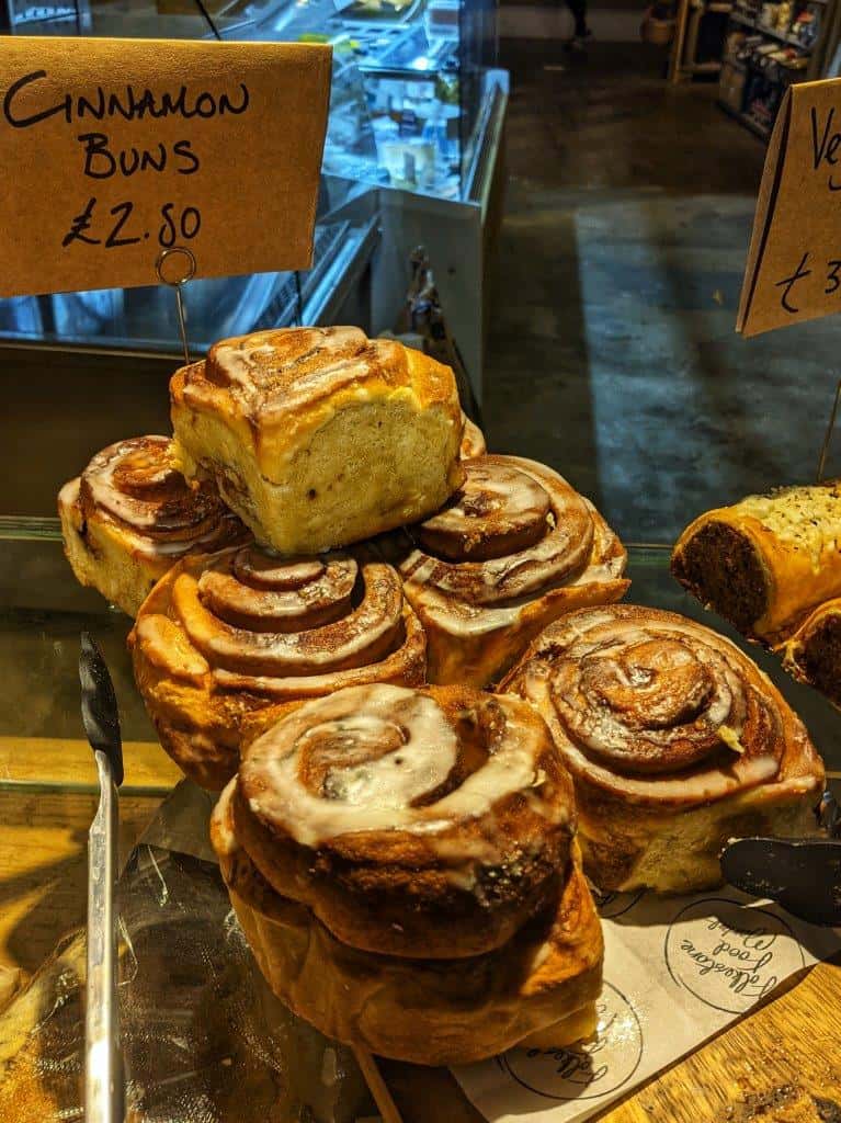 A stack of seven large and fluffy iced cinnamon buns on display in a bakery