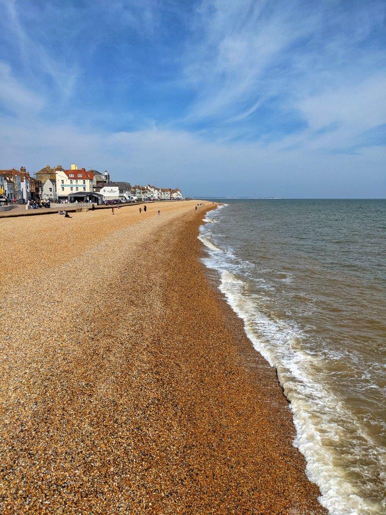 A view down a pebble beach with gently crashing waves on one side and seaside buildings on the other