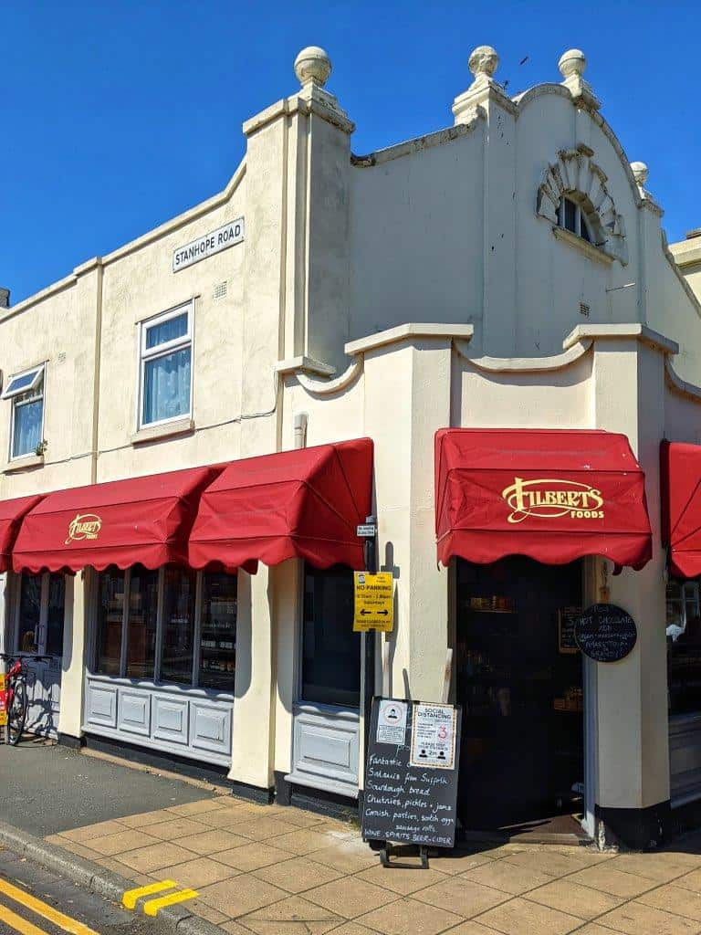 A corner view of a shop called 'Filberts Foods' with red awnings over the windows and white walls