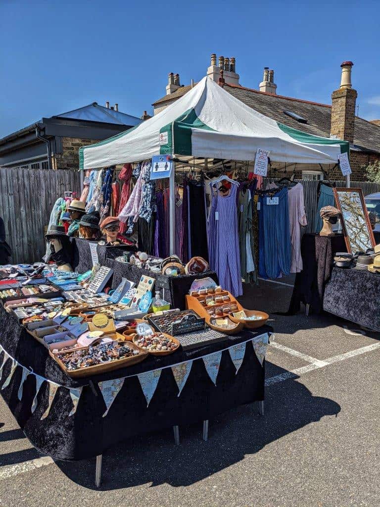 A vibrant market stall in a carpark with a table laden with trinkets and fully stocked clothing rails under a gazeebo