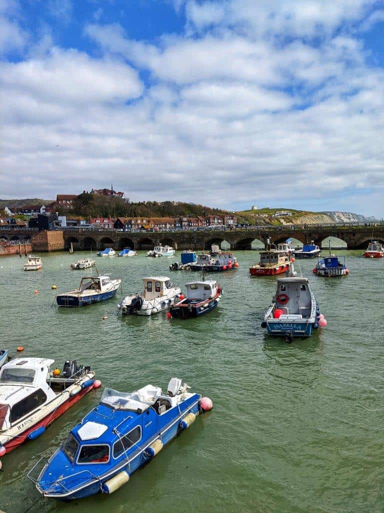 A harbour with small anchored fishing boats dotted about under a cloudy but bright sky