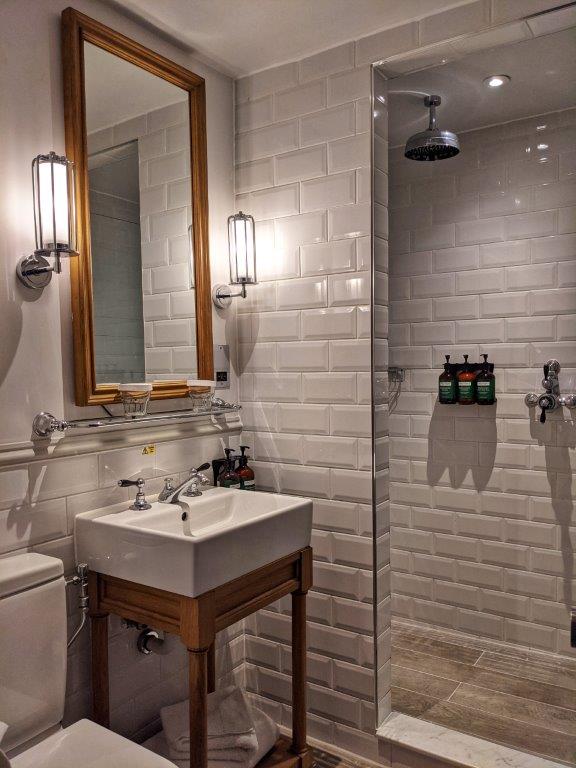 A stylish bathroom tiled white with a large walk-in shower and big mirror above the basin