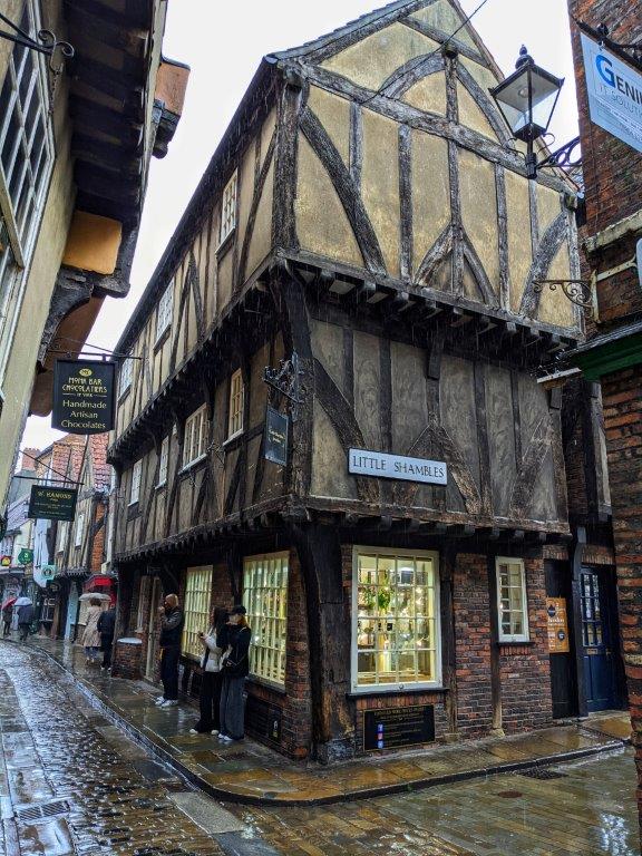 The corner of a medieval building on a cobbled street, with overhanding timber-framed upper stories