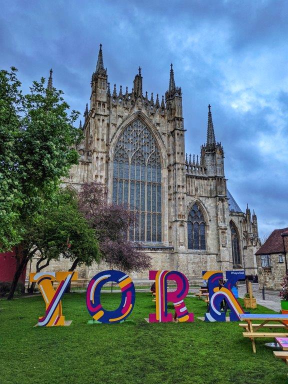 A facade of a cathedral with grass in the foreground on which four large letters read 'YORK'