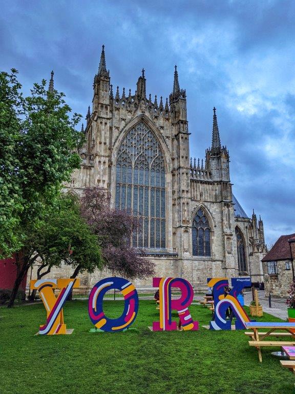 A facade of a cathedral with grass in the foreground on which four large letters read 'YORK'