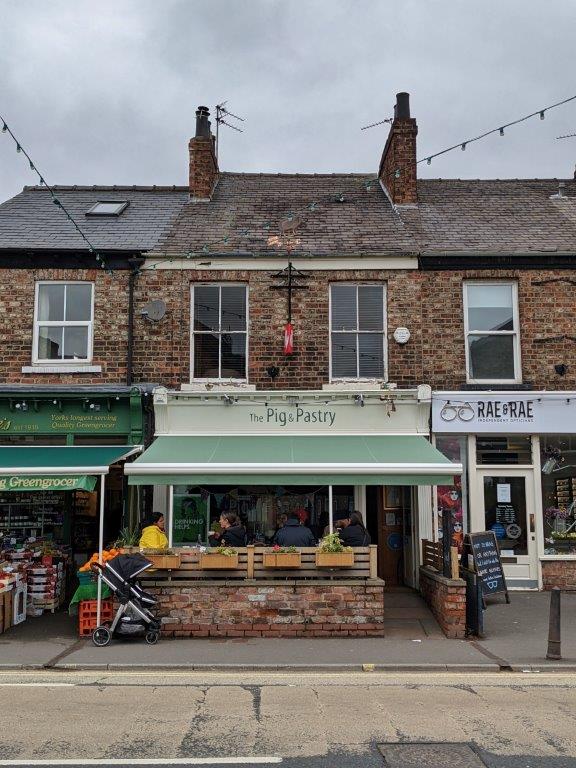 A pale green shop front with an awning, called 'The Pig and Pastry' with a few tables out the front with diners