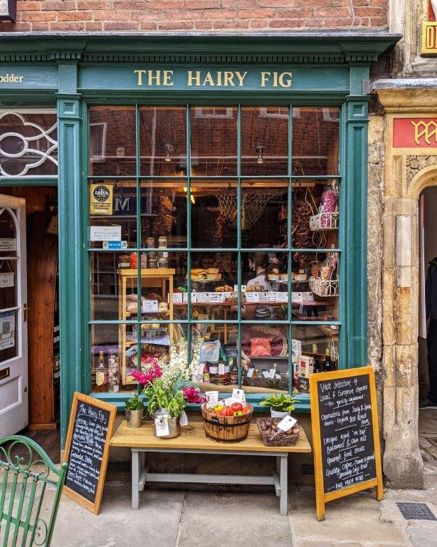 A quaint dark green shop front with lots of glass called 'The Hairy Fig' with the window filled with edible delights