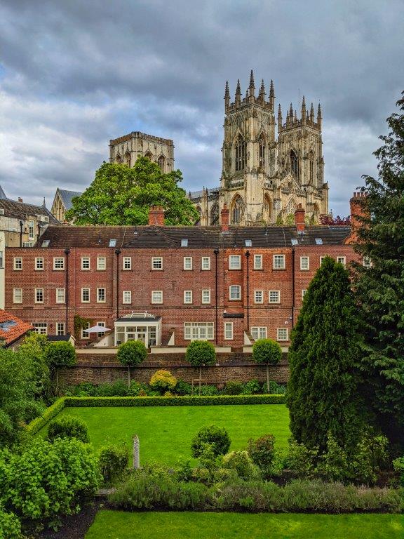 View of two towers of a cathedral in the distance, partially concealed by industrial brick buildings and a manicured lawn in the foreground