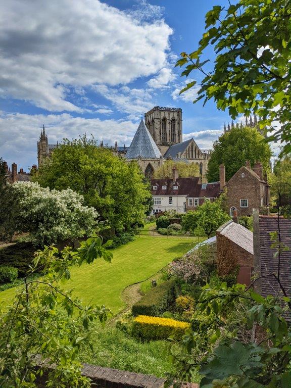 View of a cathedral partially concealed by brick buildings with a manicured lawn in the foreground