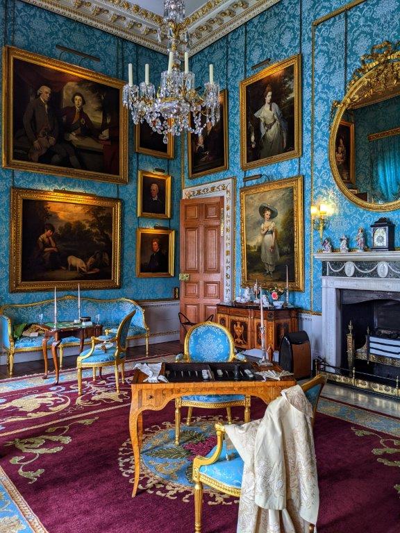 A grand room ornately decorated, with antique furniture and turquoise wallpaper and classic paintings hung on the walls