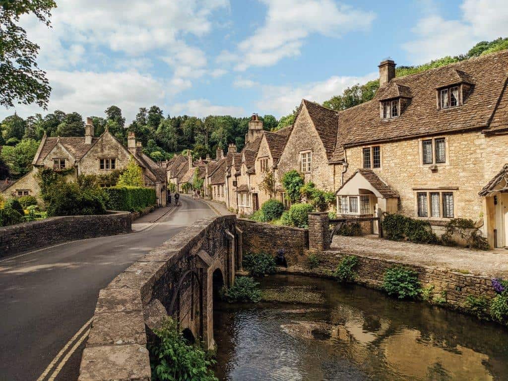 A picturesque English village road lined with old and beautiful listed houses, running over a river