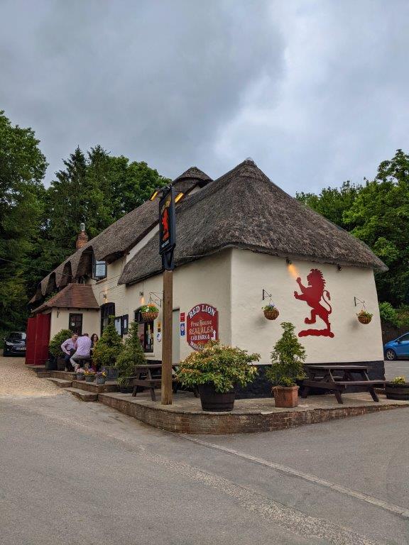 A pub with a thatched roof and a large red lion emblem on the side of the building