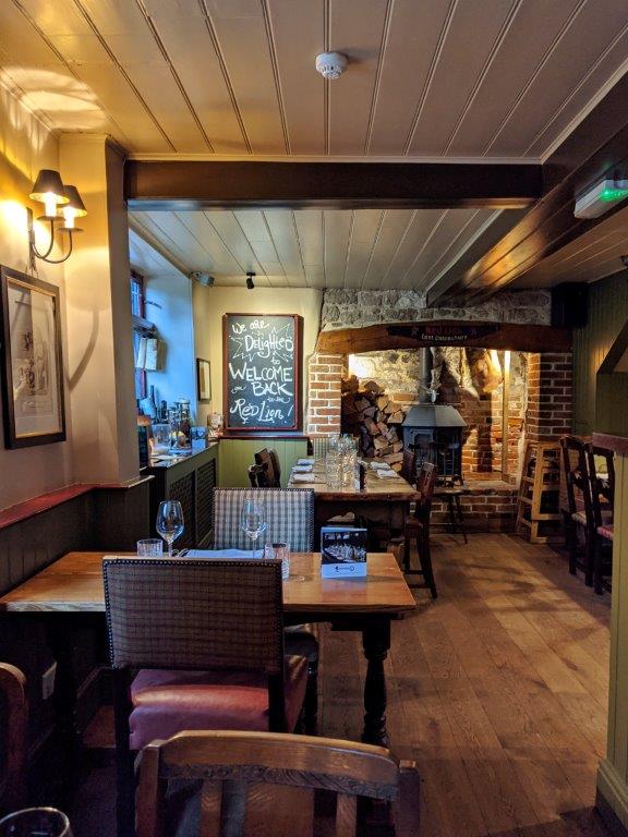 The cosy interiors of a pub with wooden floor, wood panelled ceiling and a large hearth at the back of the room