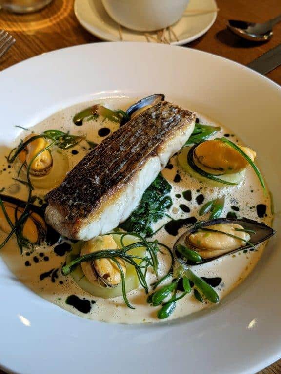 A beautiful dish of pan-fried stonebass on a bed of confit potatoes and mussels set in a shallow white bowl