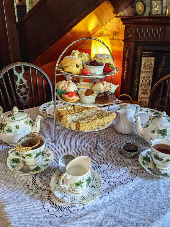 A traditional afternoon tea spread with three tiers of finger sandwiches, cakes and scones, on a lace tablecloth with a bone china tea set