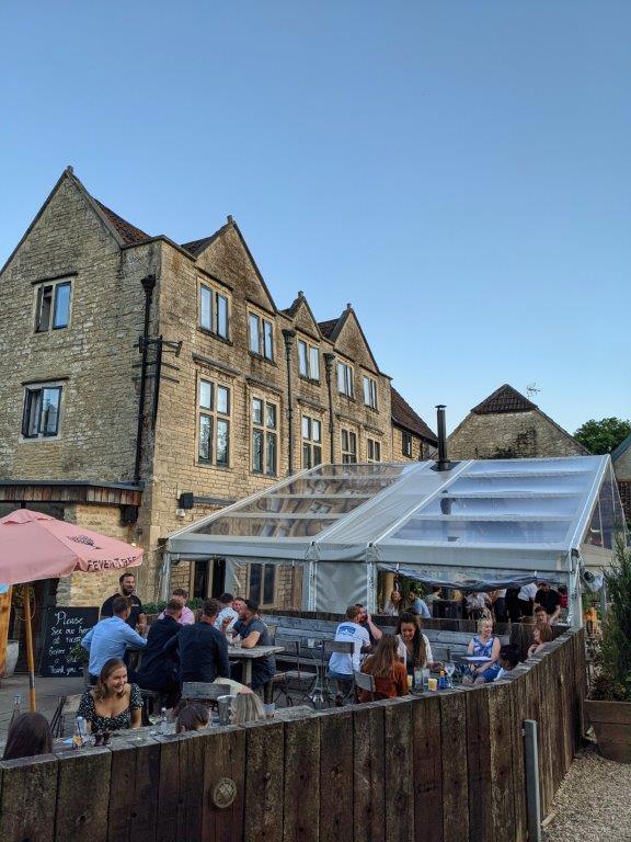 The outdoor seating area of a restaurant with patrons enjoying themselves eating and drinking under a blue sky