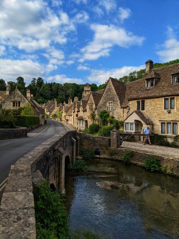 A picturesque English village road lined with old and beautiful listed houses, running over a river