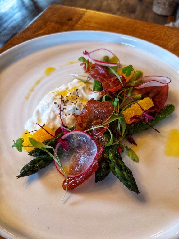 A beautifully plated dish of asparagus, burrata, crispy pancetta and orange segments